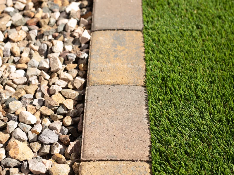 A close view of turf meeting a paver border. Rock fills the other side.