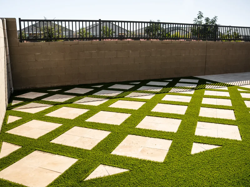 Square concrete pavers sit in a grid in a walled back yard. Turf runs between them.