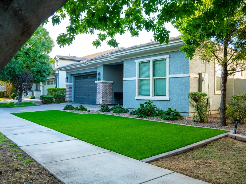 A finished turf front lawn runs along the sidewalk. The home is newer, single story, with a two car garage.