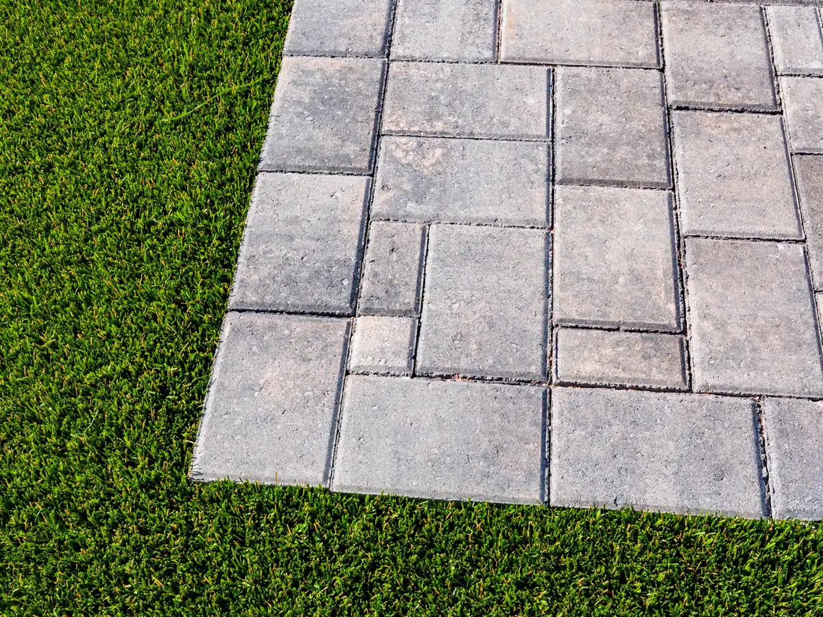 Finished artificial turf cut tight against the corner of a grey paver patio.