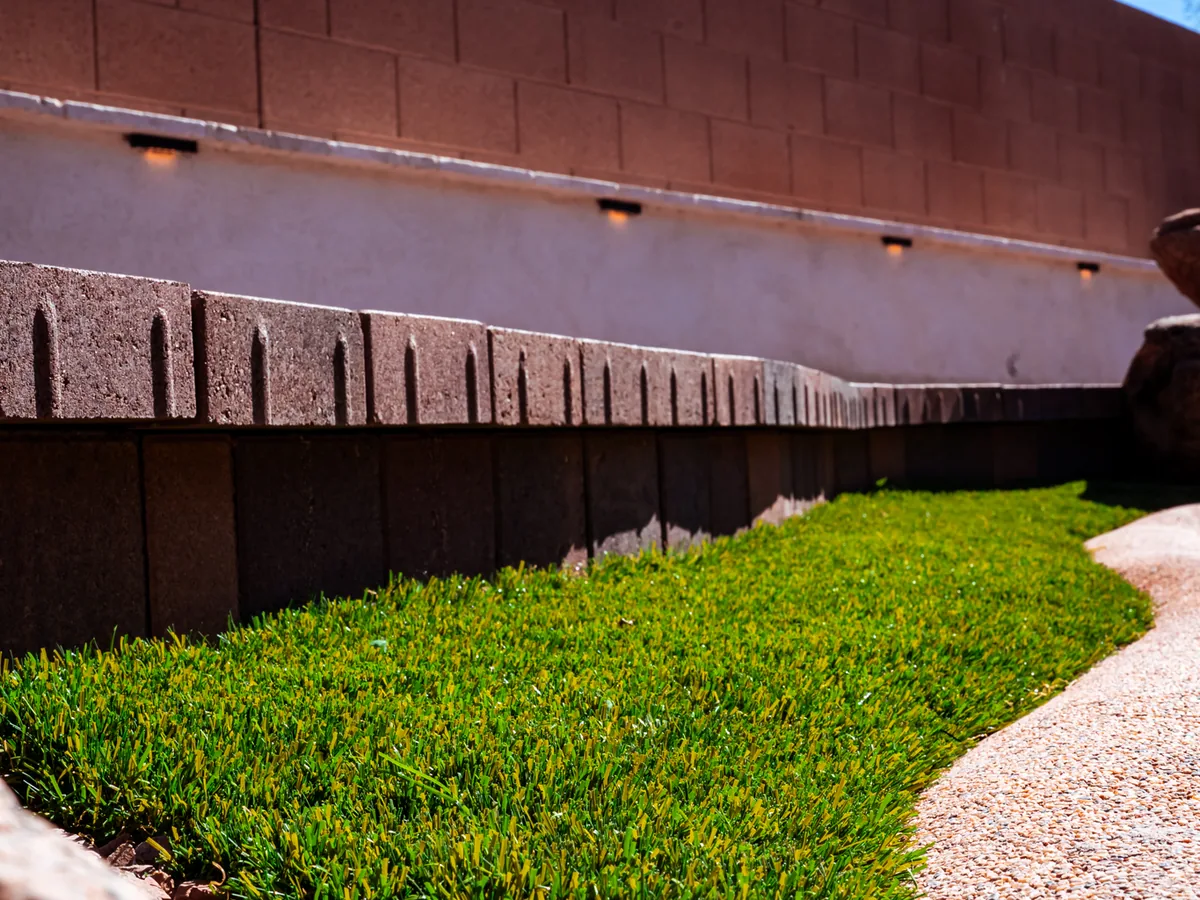 Finished turf runs tight to a concrete border. An exposed aggregate walkway runs along a block wall.