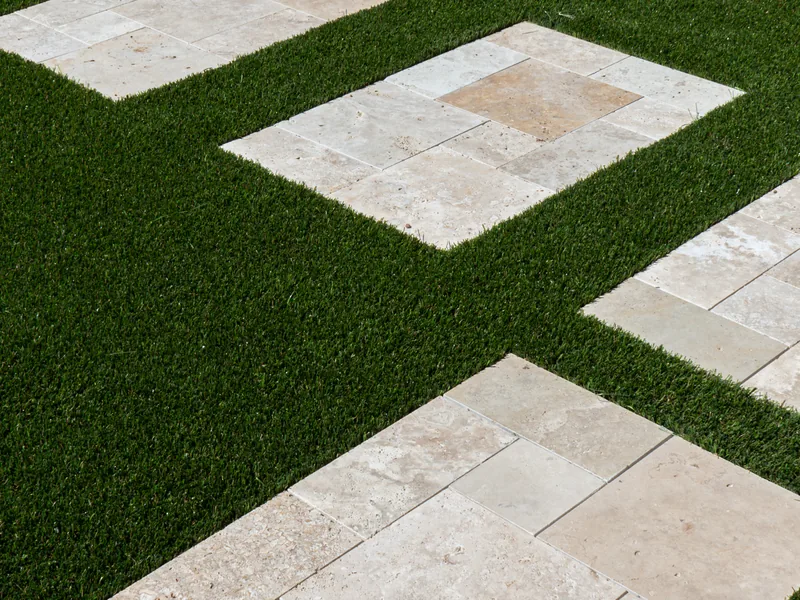 An overhead view of square pavers set into finished turf in a checkerboard pattern. The turf is cut tight around every tile.