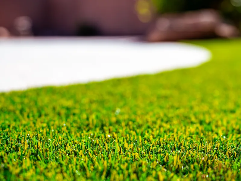 A close view at ground level of artificial turf blades meeting the curved edge of a white concrete patio.