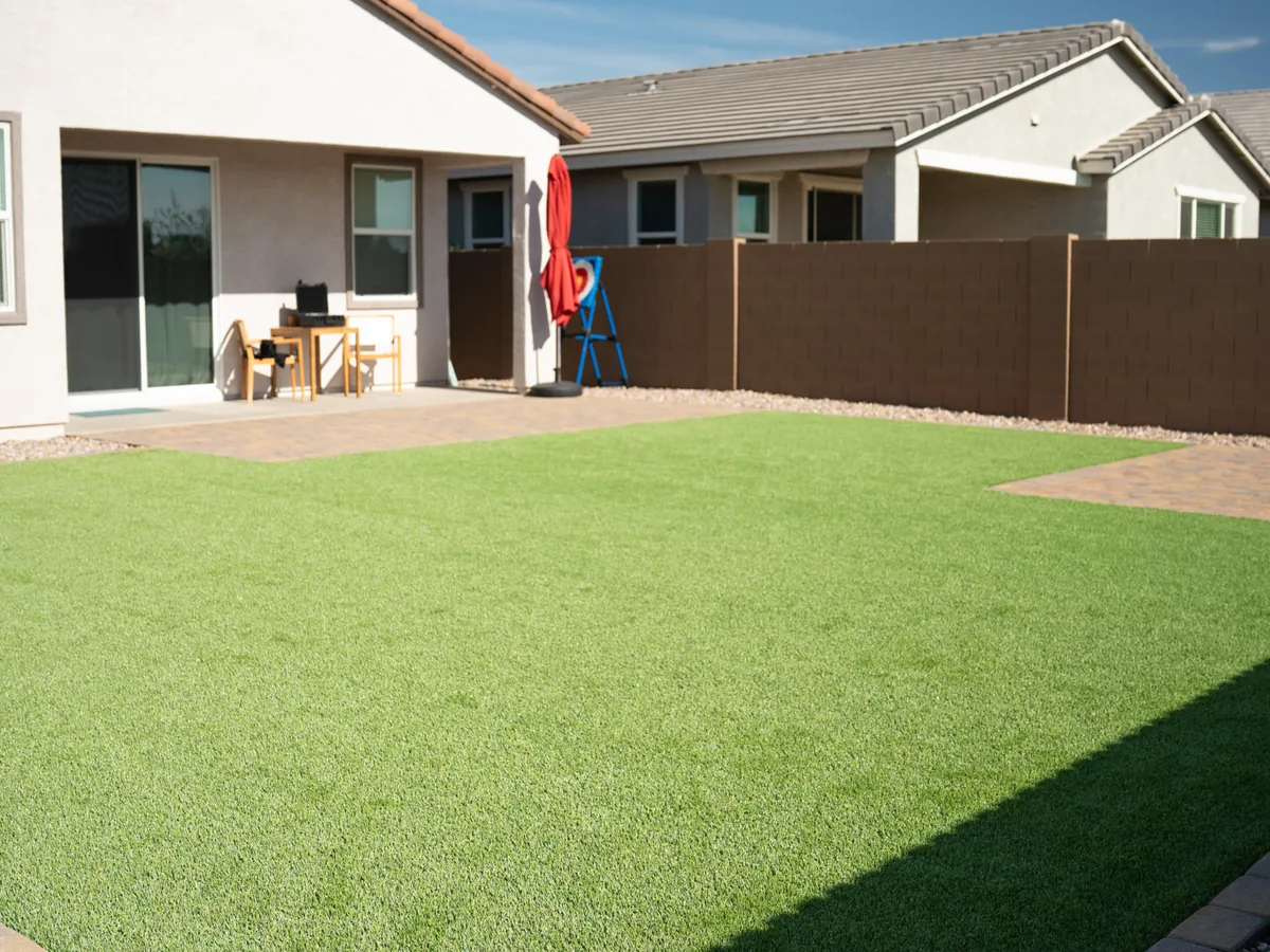 A back yard patio with a finished turf lawn, a table and chairs, and a kids outdoor game set.