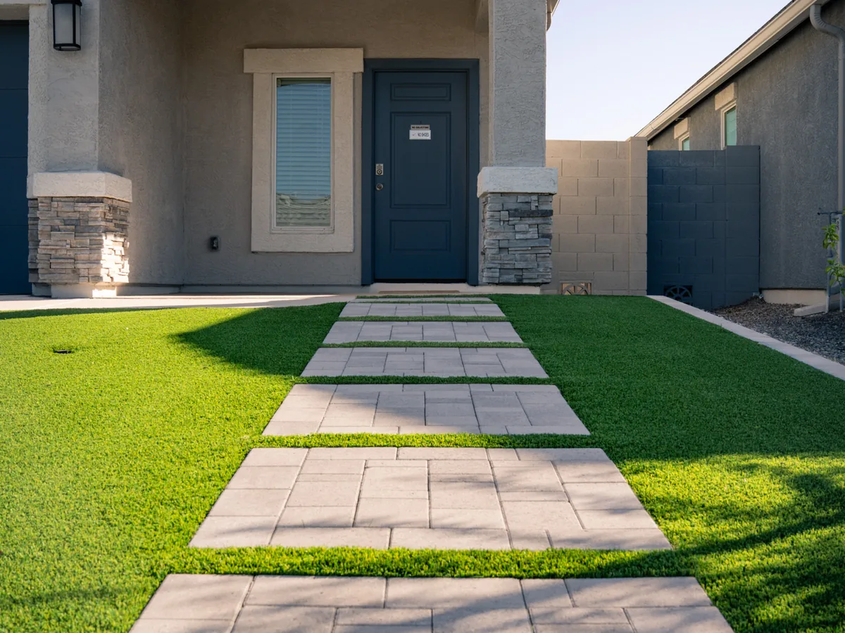 A wide paver walkway set into finished turf. It runs up to the front door of a newer stucco home.