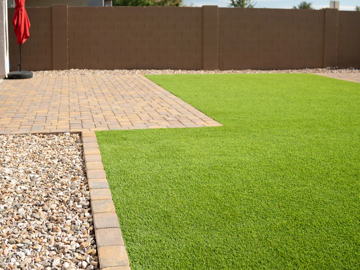 Turf running up to a paver patio, edged with a single row of pavers and a strip of decorative rock.